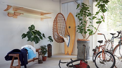 写真：部屋のインテリア。ハンモックタイプの椅子や自転車、壁にかけたサーフボード